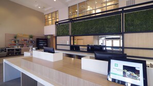 A reception area with a wooden reception desk, a digital screen displaying a discount offer, and a green vertical garden wall. - Wyndham Garden Mcallen at La Plaza Mall (McAllen)