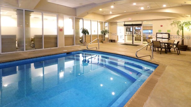 An indoor swimming pool with clear glass walls, a tiled floor, and a seating area with tables and chairs. - Wyndham Garden Mcallen at La Plaza Mall (McAllen)