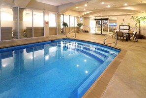 An indoor swimming pool with clear glass walls, a tiled floor, and a seating area with tables and chairs. - Wyndham Garden Mcallen at La Plaza Mall (McAllen)