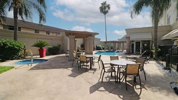 Un patio exterior con piscina, mobiliario y palmeras.