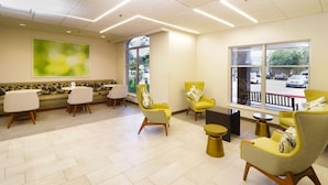A modern waiting area with a sofa, chairs, and a large window offering a view of the street. - Wyndham Garden Mcallen at La Plaza Mall (McAllen)