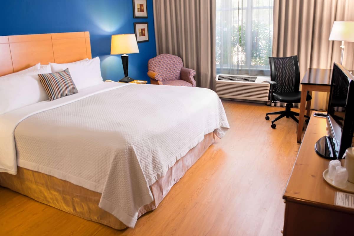 Habitación de hotel con una cama grande, un escritorio con computadora, una silla y una ventana con cortinas.