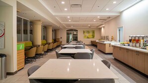 A spacious cafeteria with long tables and chairs, a counter with beverages, and a large window with a view.