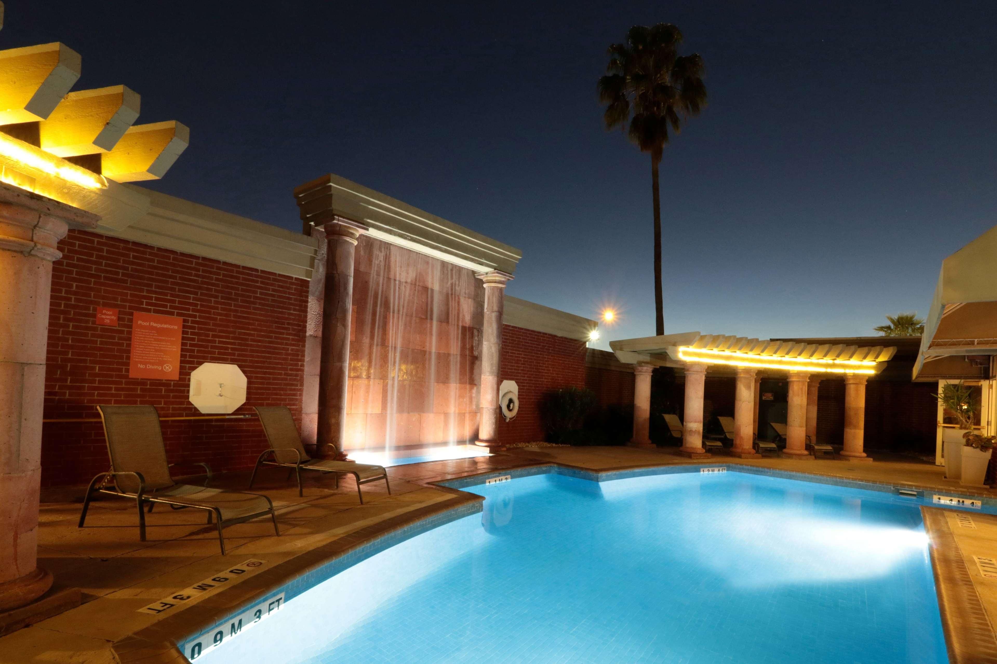 Piscina con sillas de descanso y una zona cubierta, rodeada de muros de ladrillo y columnas.