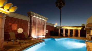 Piscina con sillas de descanso y una zona cubierta, rodeada de muros de ladrillo y columnas.