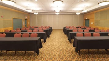 A conference room with rows of tables and chairs, carpeted floor, and ceiling lights.
