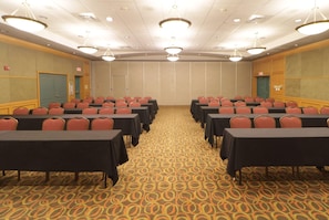 A conference room with rows of tables and chairs, carpeted floor, and ceiling lights.