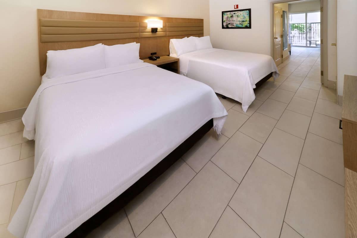 Habitación de hotel con dos camas, una mesita de noche, una lámpara de pared y una puerta que da a un balcón.