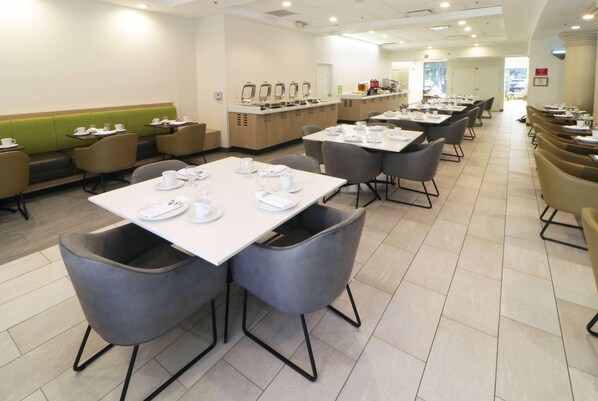 Un comedor con mesas dispuestas para comidas, una barra de buffet y asientos a lo largo de las paredes.