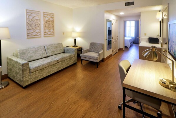 A hotel room with a sofa, armchair, desk, and lamp.