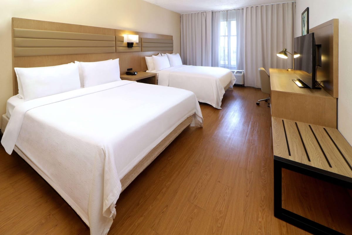 Habitación de hotel con dos camas, un escritorio, un televisor y una lámpara.