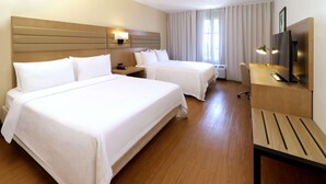 A hotel room with two beds, a desk, a TV, and a lamp.