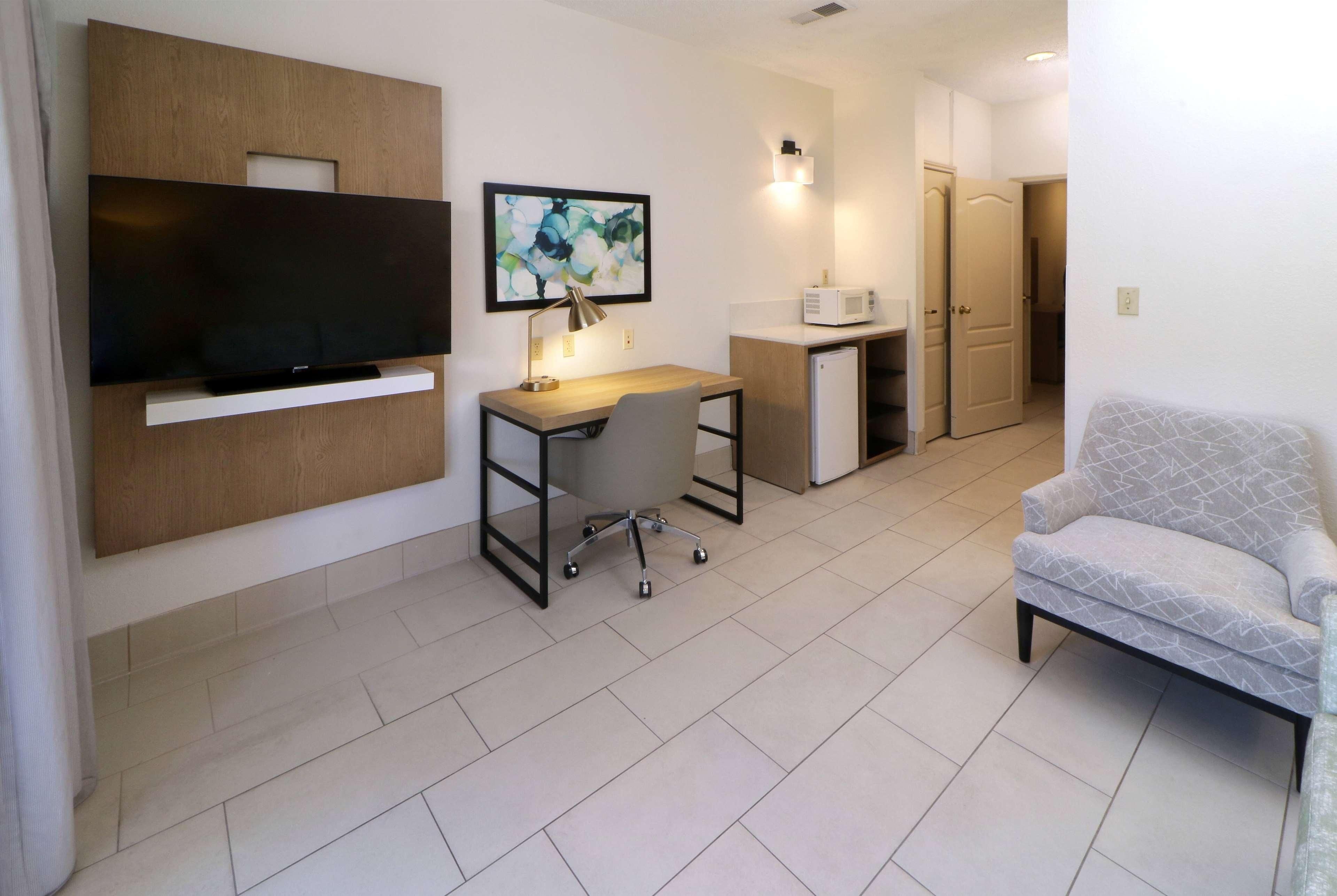 A modern living room with a flat-screen TV, a desk with a chair, a microwave, and a sofa.