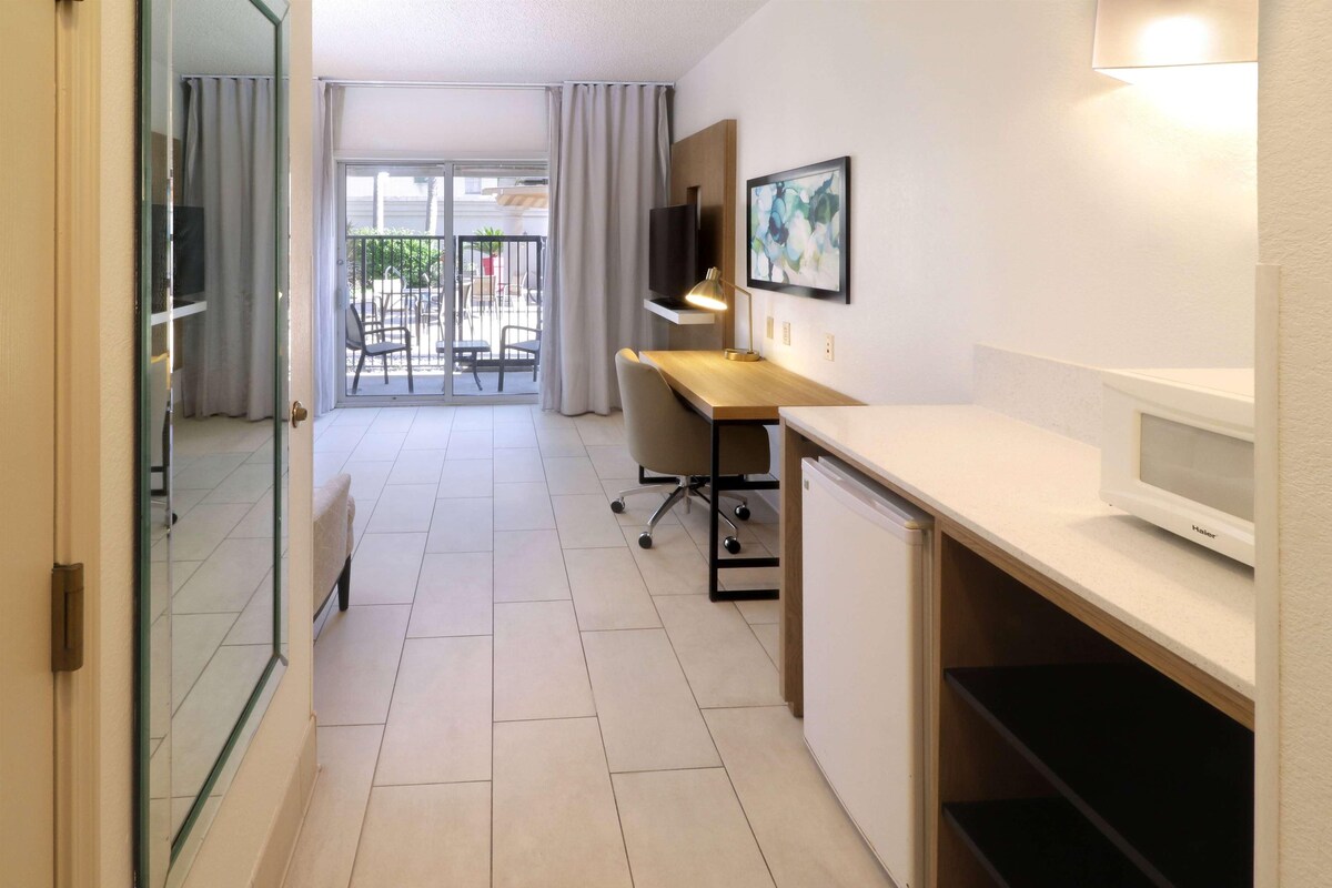 Ein modernes Hotelzimmer mit Schreibtisch, Stuhl, Fernseher und einem Balkon mit Außenmöbeln.