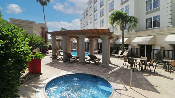 A pool area with lounge chairs, a pergola, and a building in the background.