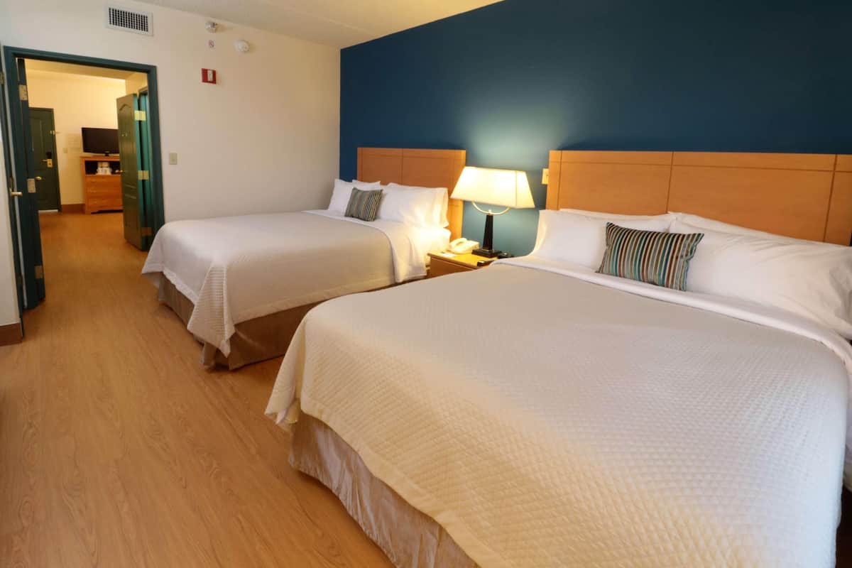 Una habitación de hotel con dos camas, una mesita de noche con lámpara y suelo de madera.