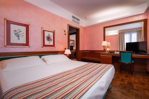 A hotel room with a large bed, a desk with a computer and TV, a chair, and framed floral artwork on the wall. - Hotel Crivi's (Milan)