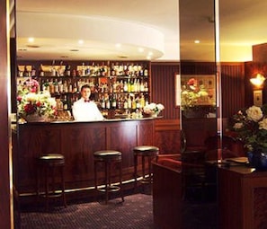 A bar area with a bartender, wooden bar counter, stools, and a wall of liquor bottles. - Hotel Crivi's (Milan)