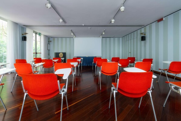 A conference room with red chairs and tables, large windows, and a projector screen. - Hotel Crivi's (Milan)