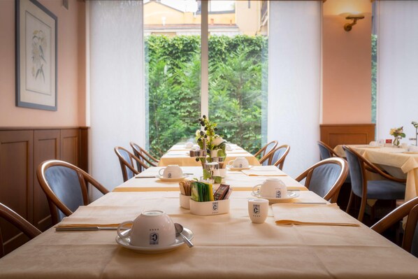 A dining table set with white tableware, a vase with flowers, and a menu stand. - Hotel Crivi's (Milan)