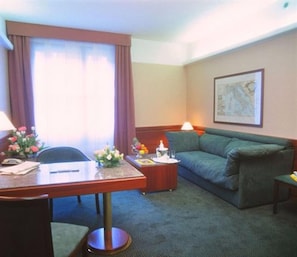 A hotel room with a desk, a green sofa, a small side table, a lamp, and a framed picture on the wall. - Hotel Crivi's (Milan)