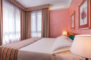 Een hotelkamer met een bed, gordijnen, een lamp en lijstwerken aan de muur.