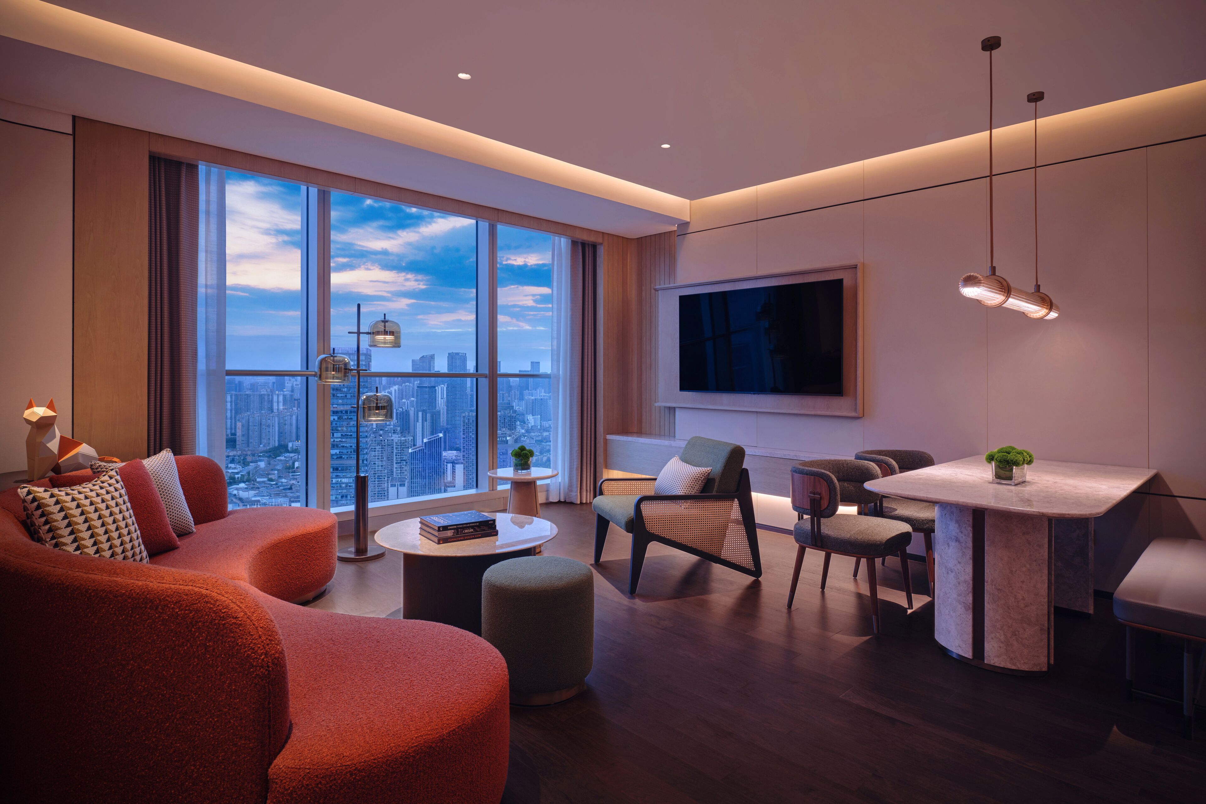 A modern living room with a large window, a dining area, and a seating arrangement.
