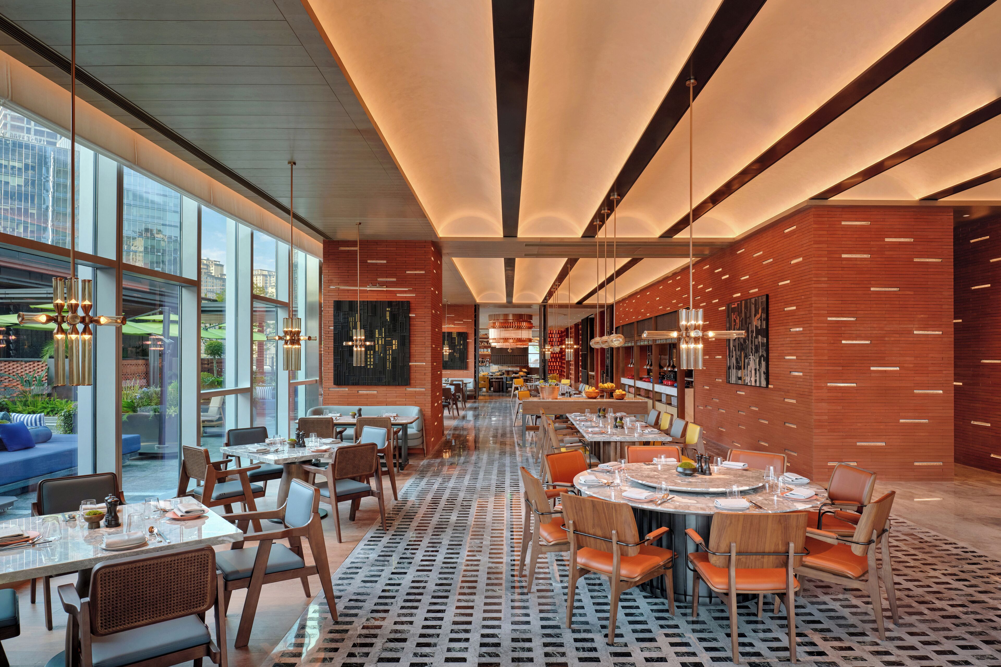 A modern restaurant with high ceilings, large windows, and a patterned floor. Tables are set with chairs and dining ware.