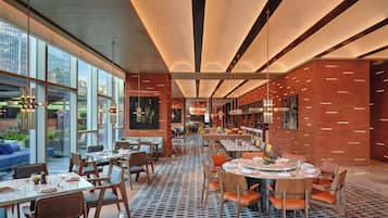 A modern restaurant with high ceilings, large windows, and a patterned floor. Tables are set with chairs and dining ware.
