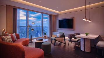 A modern living room with a large window, a dining area, and a flat-screen TV mounted on the wall.