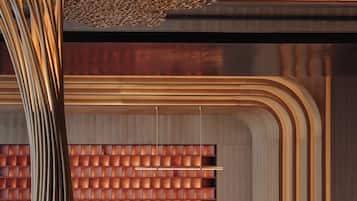 Un espace d’accueil moderne avec un comptoir en bois, une grande structure décorative en forme d’arbre et un mur orné d’un motif derrière le comptoir.