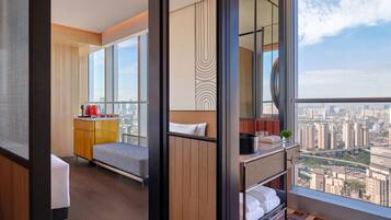 Ett modernt hotellrum med ett stort fönster, en säng, ett litet pentry och utsikt över stadsbilden.