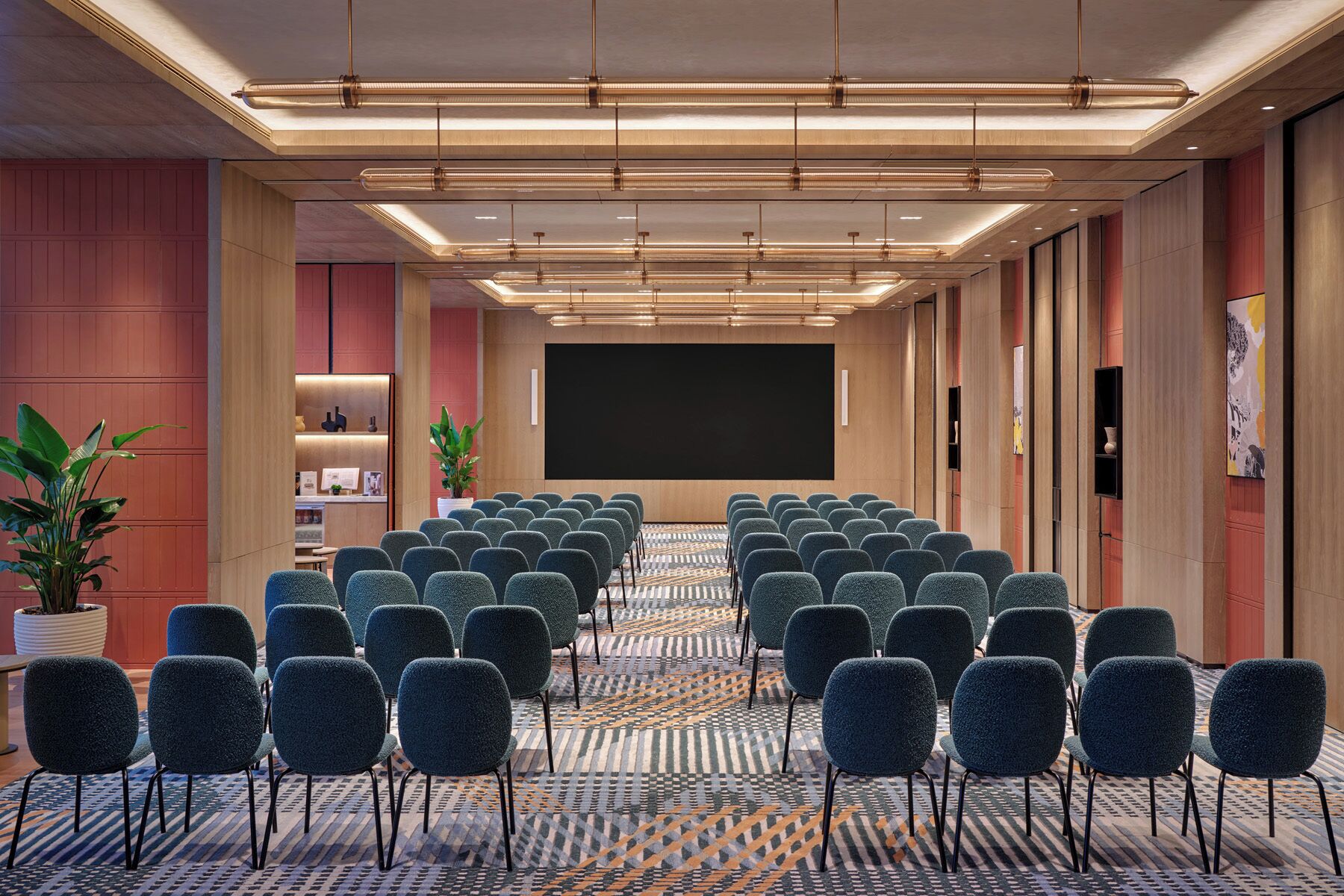A conference room with rows of chairs, a large screen, and a patterned carpet.