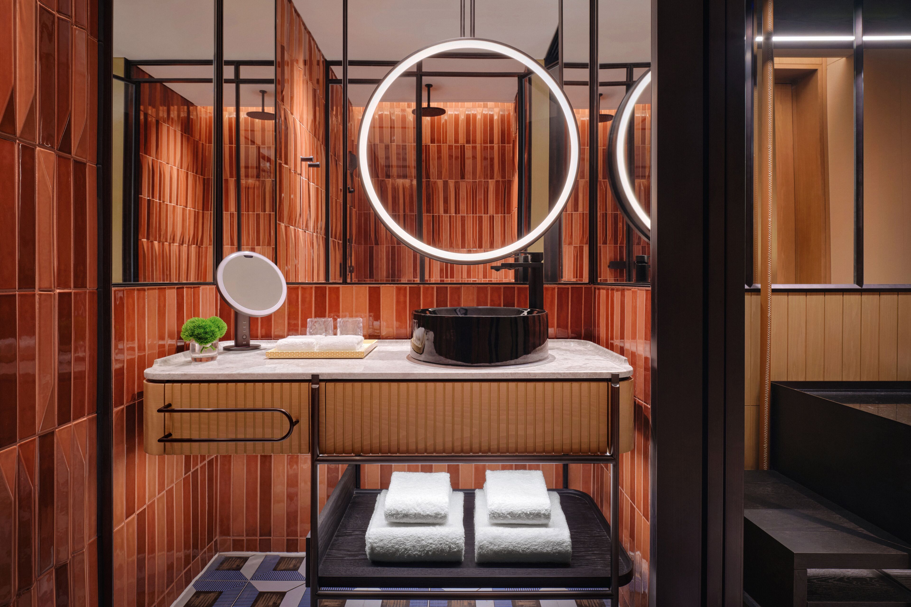 A modern bathroom with a wooden vanity, a round mirror, and a towel rack.