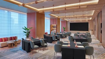 A conference room with tables, chairs, a large screen, and a patterned carpet.