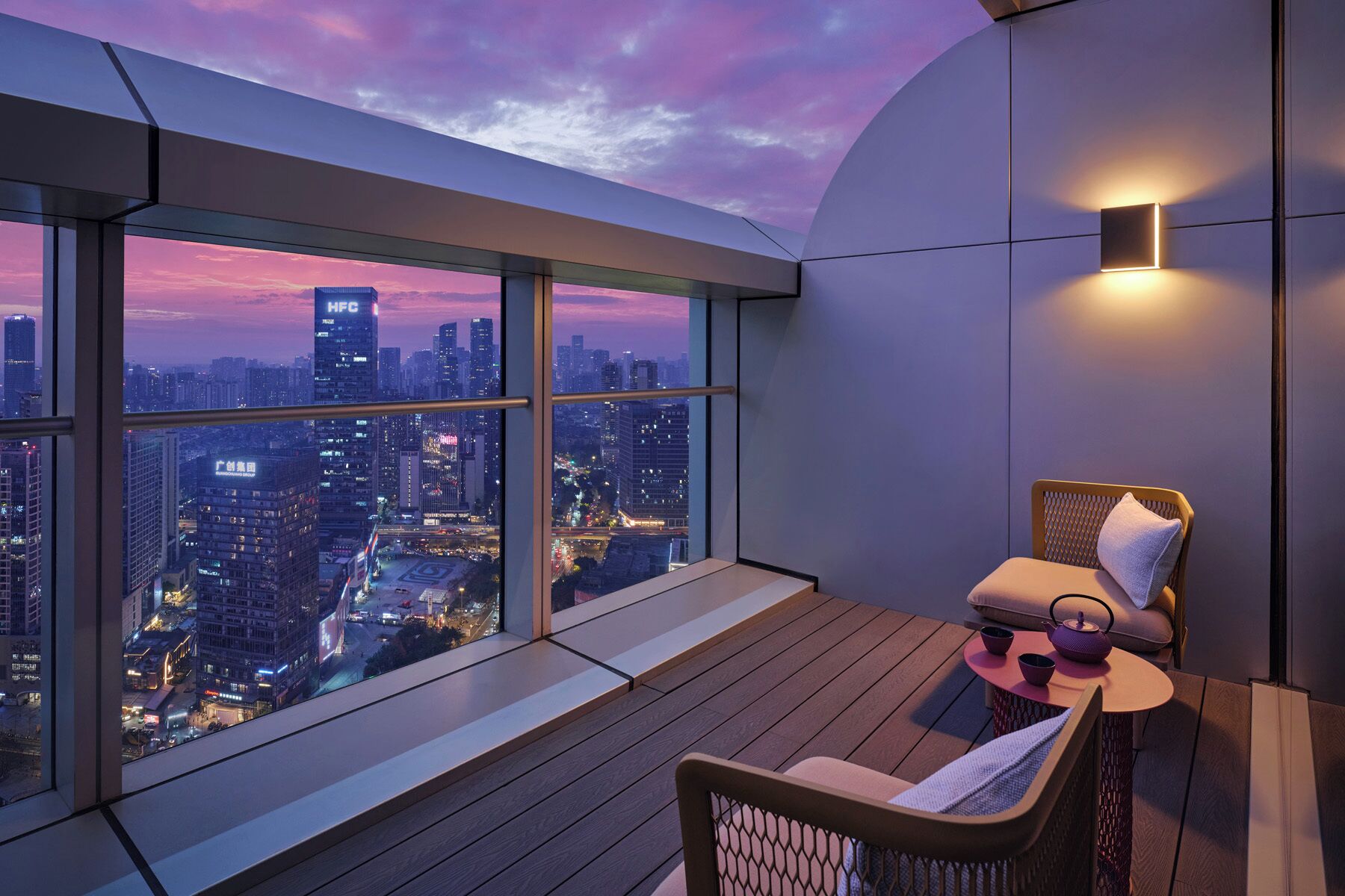 Varanda com vista para a cidade, área de estar acolchoada e uma pequena mesa com chaleira.