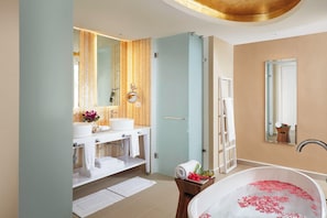 Un baño moderno con dos lavamanos, una bañera con pétalos de rosa, un perchero y un espejo.
