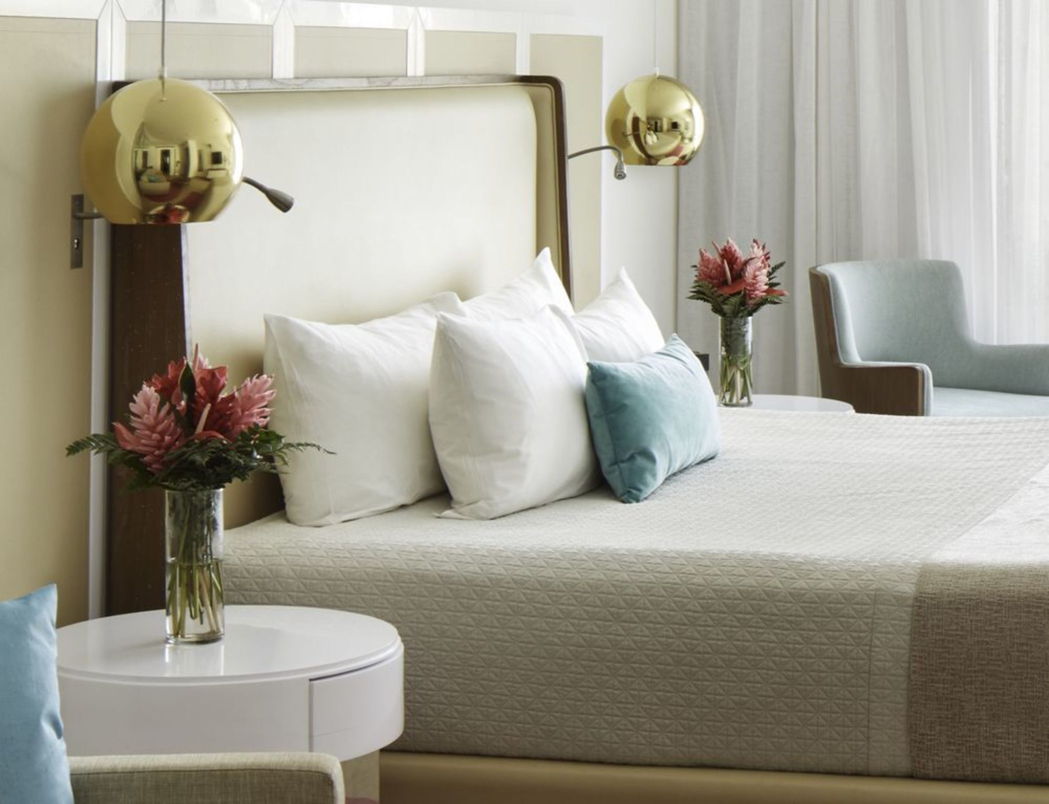 A hotel room with a bed, two bedside tables, a chair, and a large mirror with two spherical lights.