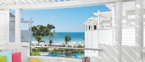 Un balcón con vista al océano, una piscina y una mesa con una bebida y fruta.