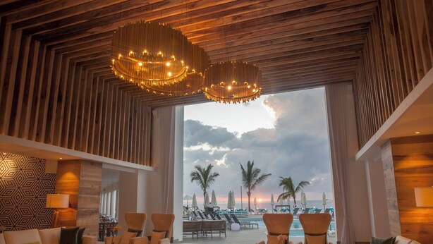 Un hall d’entrée spacieux, doté d’une grande fenêtre donnant sur une plage, aménagé avec des canapés et des fauteuils, et caractérisé par un plafond en bois et un mur orné de motifs.