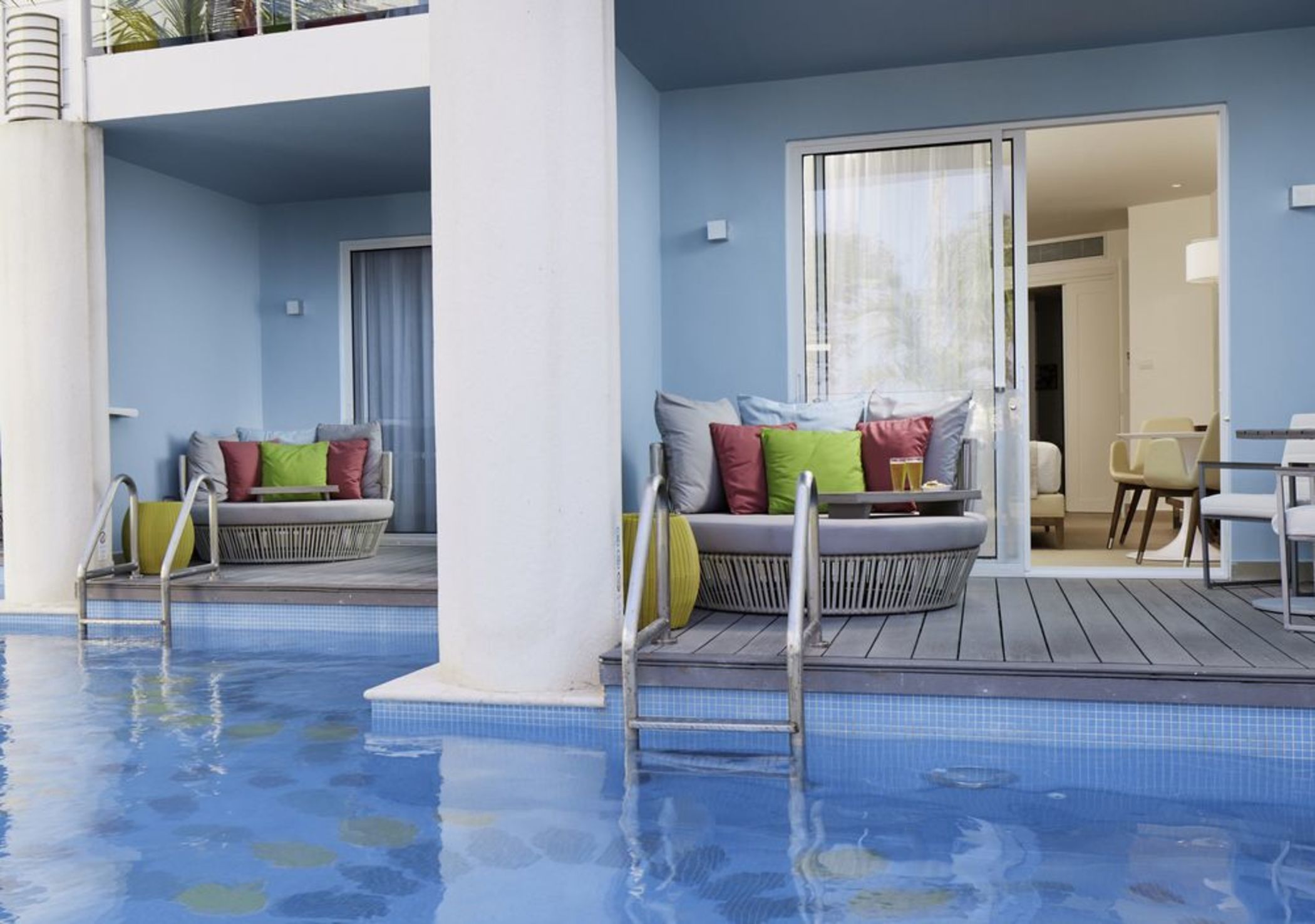 A pool area with two seating areas, each with a set of colorful cushions and a small table.