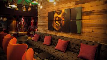 A modern lounge area with a tufted sofa, orange chairs, and pendant lighting.