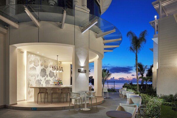 A modern bar area with a curved glass railing, a bar counter, and seating. - Azul Beach Resort Negril By Karisma (Negril)