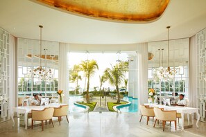 Amplio espacio interior con vista a la piscina, que cuenta con dos estaciones de trabajo con computadoras, mobiliario blanco y un diseño de techo moderno.