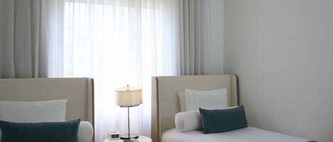 A hotel room with two beds, a nightstand with a lamp, and a window with curtains.