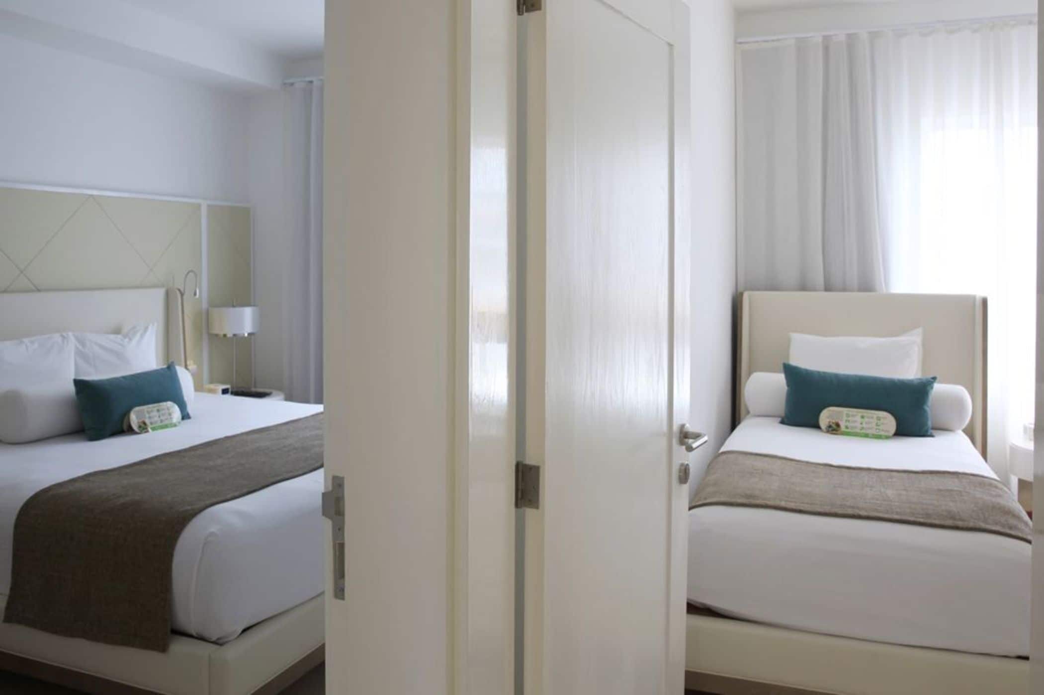 Two adjacent hotel rooms with beds, nightstands, and curtains.