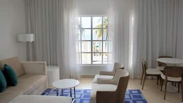 A modern hotel room with a sofa, a round coffee table, a dining set, and a large window with curtains.
