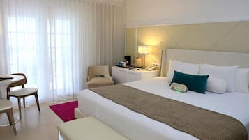 A hotel room with a large bed, a desk, a chair, a nightstand, and a lamp.