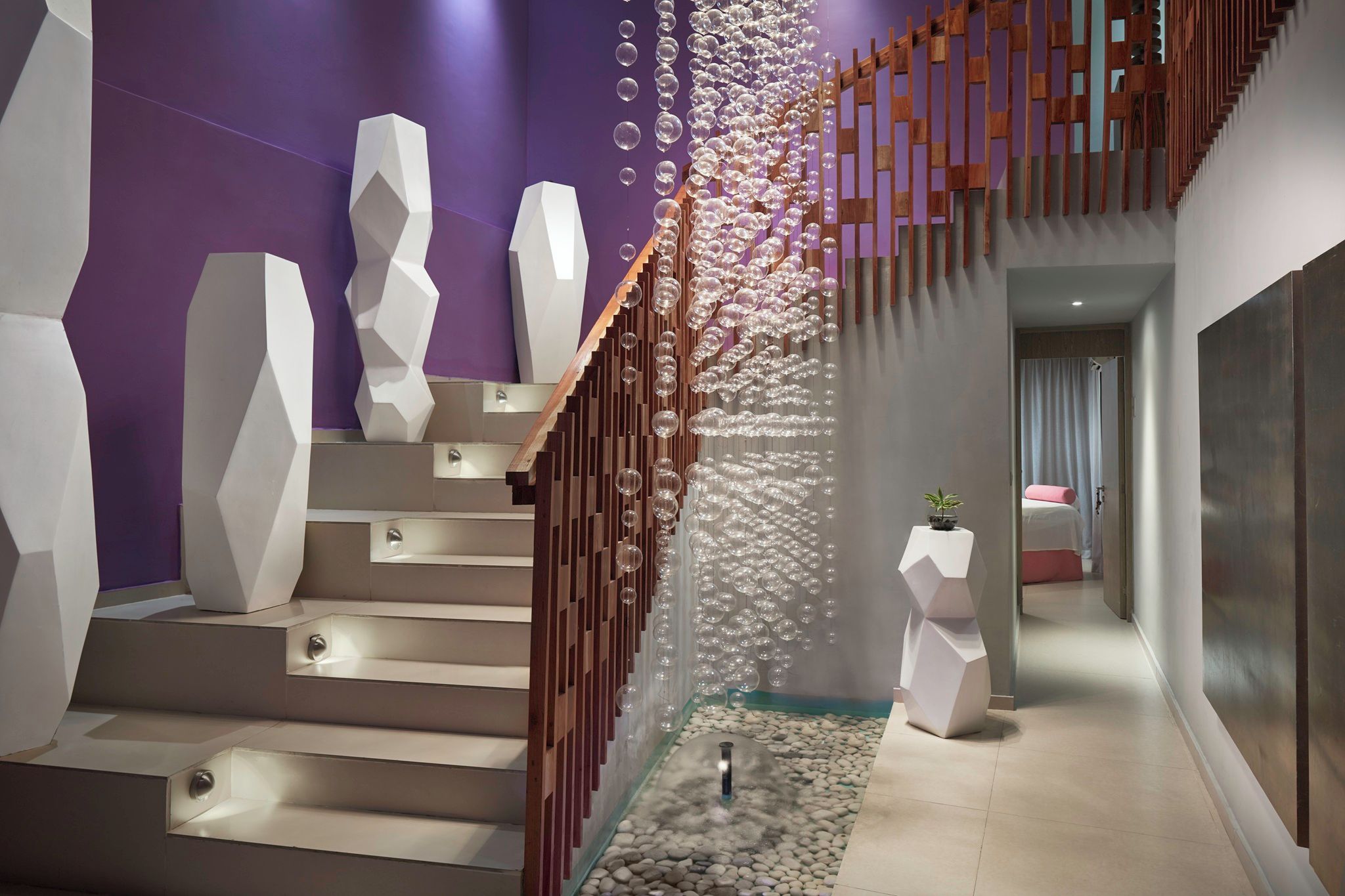 A modern staircase with geometric white steps and a wooden railing, leading to a room with a purple wall and a decorative bubble wall.
