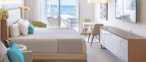 Habitación de hotel con cama, sofá, escritorio y televisión. Tiene un balcón con vistas al mar.